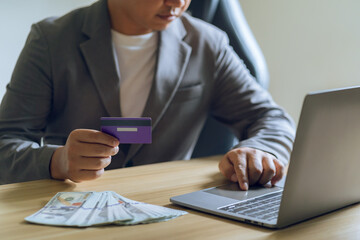 Businessman's hand holds a credit card and uses a laptop to calculate expenses.