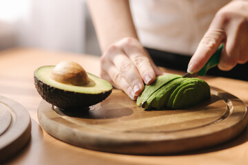 Woman slice avocado on wooden board. Second half of an avocado with pit