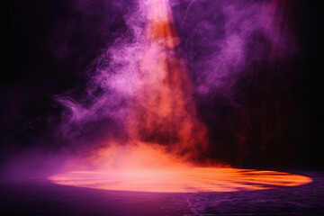 A stage bathed in pale lavender smoke under a dark orange spotlight, setting a mysterious mood against a black background.