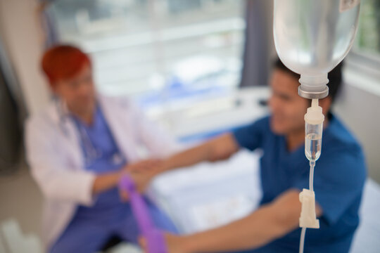 An iron stand to hang saline bottle high to deliver saline via catheter to an intravenous patient lying on patient bed. Medical concept in which doctor gives saline solution to patient through vein