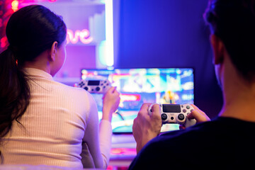Couple joyful player video game on TV using joysticks at back side, playing fighting game with...