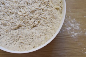 bowl with yeast dough on the wooden kitchen table.