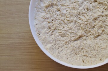 a bowl with yeast dough on the wooden kitchen table.