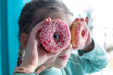 Portrait of a cheerful young European girl holding two donuts over her eyes