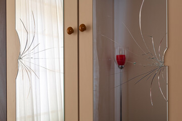 Broken mirrors on the wardrobe door. Reflection of tulle curtain and red lampshade in the mirror. Male violence, violence against women, domestic violence concept.