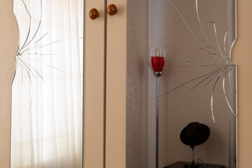 Broken mirrors on the wardrobe door. Reflection of a tulle curtain, a red lampshade and a man's hat...