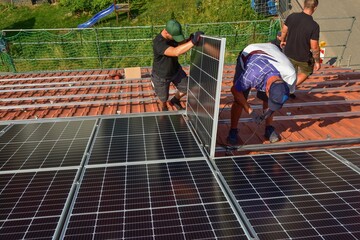 Dachdecker beim Aufbau einer Photovoltaikanlage auf einem neu gedeckten Ziegeldach: Während der...