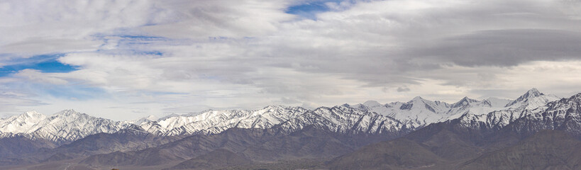 A panoramic view of snow-covered mountain ranges with clouds in the sky at Ladakh 