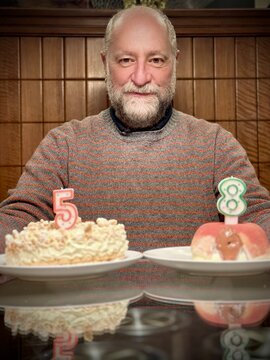 Smiling man sitting at a table with two birthday cakes with the numbers 5 and 8