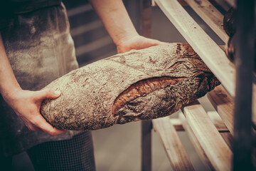 Female baker puts freshly baked bread on a wooden shelf