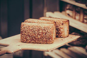 Freshly baked bread is pushed into a wooden shelf cart in a bakery using a wooden pusher - obrazy, fototapety, plakaty