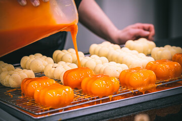 Confectioner's hand covering tartlets with an orange glaze.