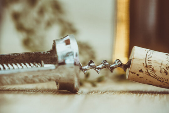 Close-up of a metal corkscrew with bottle opener next to a cork on a table