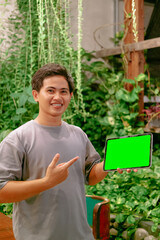 Young Asian Man Pointing at iPad or Tablet with Green Screen in Cafe Background