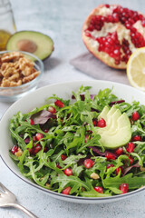 A plate with green rocket salad with pomegranate and avocado	