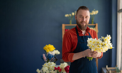 A florist creating a beautiful bouquet of spring daffodil flowers works in his flower shop. Small...