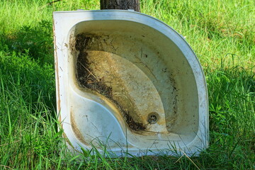 one plastic old white dirty discarded broken small bathtub lies on the green grass near a tree on...