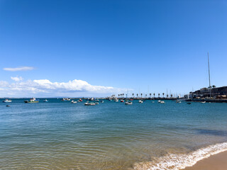Obraz premium Calm beach with crystal clear water and boats in the background.