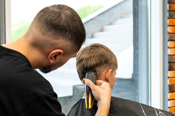 Fototapeta premium A child with very beautiful blond hair is in a barbershop and is being milled with a special hair milling machine.