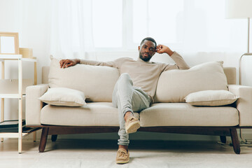 A Relaxed African American Man Sitting Alone on a Comfortable Sofa in a Modern Living Room, Deep in Thought and Contemplation