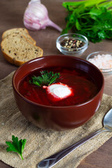red beet soup. brown bowl of soup with spoon. delicious borscht with sour cream, garlic, green parsley. Traditional Russian and Ukrainian dish on a wooden background. copy space. vertical
