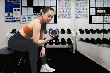 A woman is lifting a dumbbell in a gym. A mature woman is lifting a dumbbell in a gymnasium to build muscle and keep her body fit.