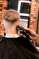 Professional barber using an electric shaver or trimmer to neaten the modern V-shaped hairstyle of...