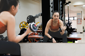 A woman is lifting a dumbbell in a gym. A mature woman is lifting a dumbbell in a gymnasium to build muscle and keep her body fit.