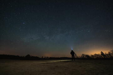 Night outdoor scene in Estonia. A man with a headlamp admires the stars.