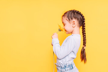 A child smells a yellow flower against a yellow background.