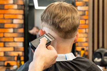Barber cuts red-haired client occiput with adjustable trimmer in barbershop closeup. Professional...