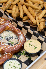 Large salted pretzel on checkered paper with dipping sauces. Close-up photograph jpg.