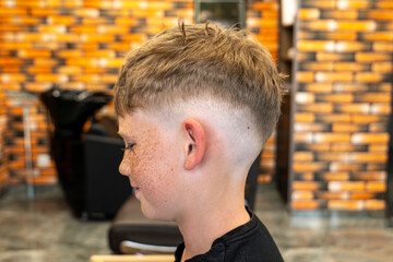 The picture of a small child in a barbershop studio, taken from the side and enjoying the beautiful...