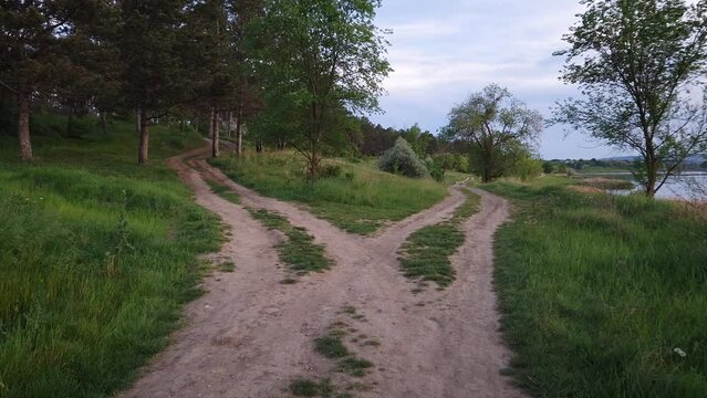 Split country road scene. Crossroad concept choosing the way. Idyllic summer rural landscape and two dirt tracks in the nature leading to the forest and the lake