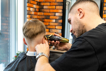 the process of hair styling a blond boy with with hair dryer and comb in a chair in a barbershop...