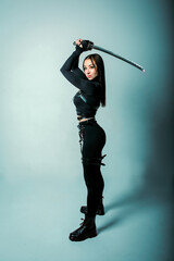 A young ninja woman in a black suit with a toned figure with a katana in her hands raised up stands...