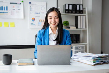 A woman is sitting at a desk with a laptop and a stack of papers