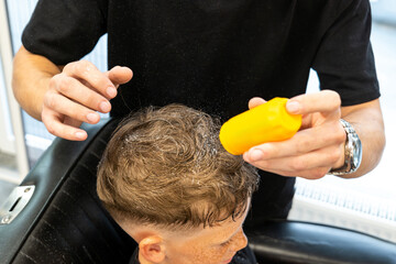 Professional hairdresser barber using talcum powder for his client hair sitting in a barber chair...