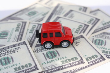 A small car against the background of money. Toy car and scattered dollars. Concept of buying, selling, costs, car repair.
