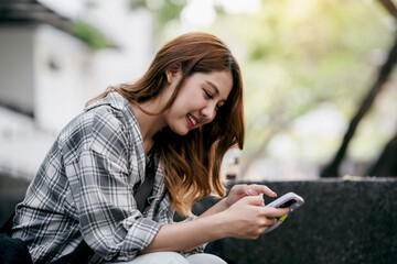 Fototapeta premium A woman is sitting on a bench and looking at her cell phone