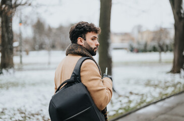 Thoughtful bearded man with backpack walking in a snow-covered winter park.
