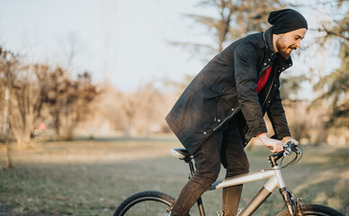 A casual male cyclist rides a bicycle in a park during a sunny afternoon, embodying relaxation,...
