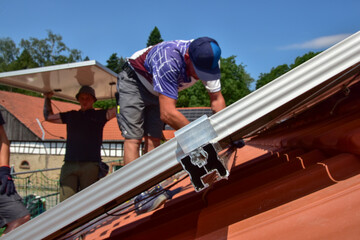 Dachdecker beim Aufbau einer Photovoltaikanlage auf einem neu gedeckten Ziegeldach: Die Endklemmen...