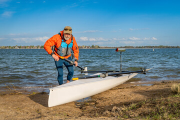 Senior male rower with his rowing shell on a beach of Boyd Lake in northern Colorado, early spring...