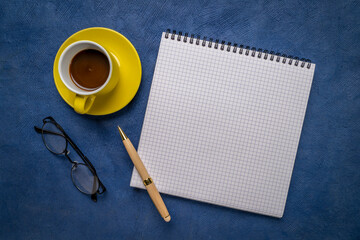 blank spiral notebook with ruled paper, flat lay with coffee, reading glasses and pen on blue textured art paper