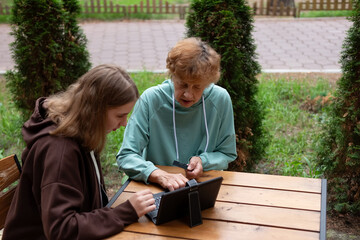 computer awareness of the elderly. a happy teenage girl teaches older 70s grandmothers to use a...