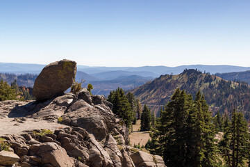 a big rock at a hillside cliff in front of a beautiful panoramic Mountain View into the valley of lassen volcanic national park, california