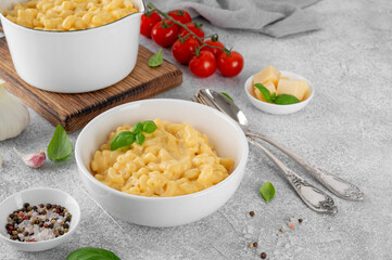 Mac and cheese in a white bowl with fresh basil on top on a gray concrete background. American cuisine, comfort food. Copy space.