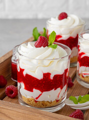 Raspberry trifle with whipped cream, berry sauce, cookie crumbs and mint leaves in a glass on a wooden tray. Summer diet dessert.