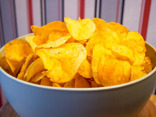 Crispy Potato Chips. A bowl of golden potato chips against a striped backdrop, perfect for snack content.